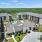 Land O' Lakes, FL, Townhomes - Everwell at Bexley - Aerial View of Property Showing White Walls and Grey Roofing, Pool Area, Landscaped Grounds, Trees, Forest, and Lake.