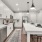 Townhouses in Land O' Lakes, FL - Everwell at Bexley - Kitchen with Wood-Style Flooring, Stainless Steel Appliances, Quartz Countertops, White Tile Backsplash, White Cabinetry, Large Island with Chairs, and Pendant Lights.