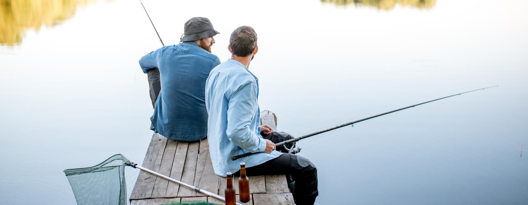 two men sit on a dock and fish